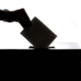 Eine Hand wirft einen Zettel in eine Wahlurne.