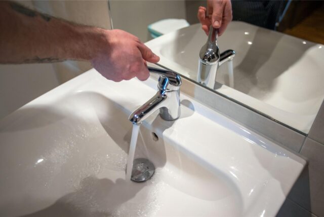 Eine Person lässt das Wasser an einem Waschbecken laufen.
