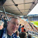Axel Tschersich sitzt mit Fanschal auf einer Tribüne des ausverkauften Bochumer Ruhrstadions.