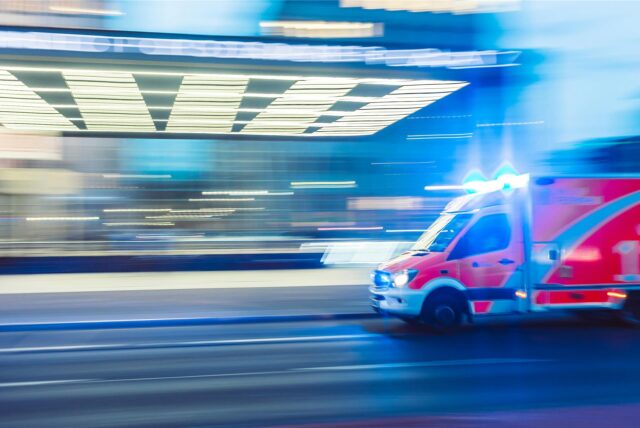Ein Krankenwagen mit Blaulicht fährt an einer Straße vorbei.