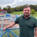 Dennis Cornelius steht auf dem Außengelände des Copa Ca Backum. Links hinter ihm sind die Wasserrutschen des Spaßbads zu sehen. Er lehnt an einem Geländer.