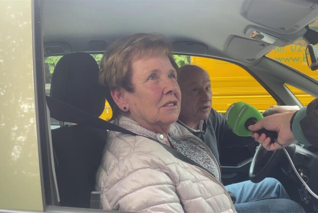 Ein Ehepaar sitzt im Auto, ein Reporter hält ein Mikrofon hinein und führt ein Interview.