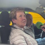 Ein Ehepaar sitzt im Auto, ein Reporter hält ein Mikrofon hinein und führt ein Interview.