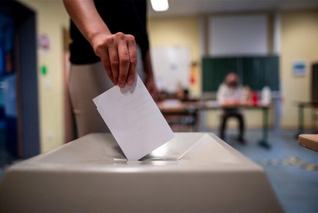 Eine Frau wirft einen Wahlschein in eine Wahlurne.