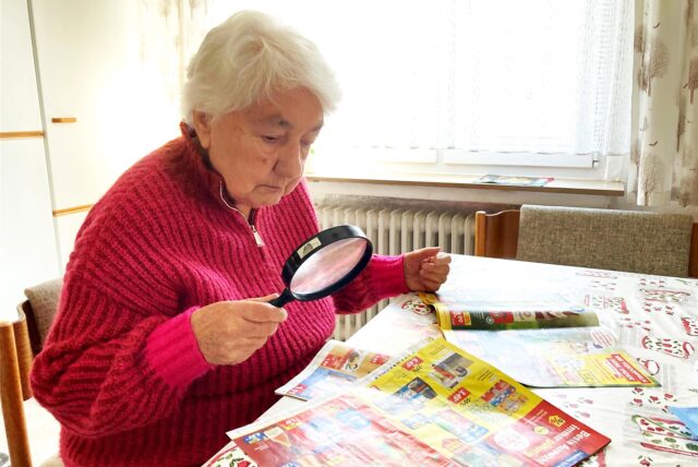 Die Hertenerin Gisela Riepenhoff blickt beim Lesen von Prospekten durch eine Lupe.
