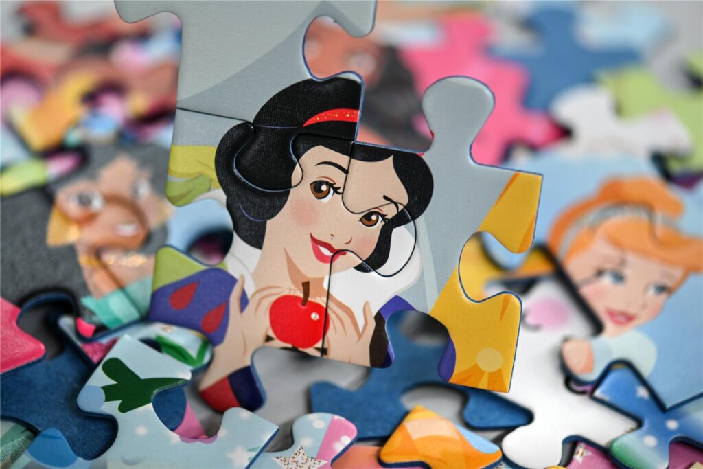 Mehrere Teile eines Disney-Puzzles liegen auf einem Tisch, davor sind drei Teile mit dem Gesicht von Schneewittchen zusammengefügt. Mehrere Teile eines Disney-Puzzles liegen auf einem Tisch, davor sind drei Teile mit dem Gesicht von Schneewittchen zusammengefügt.