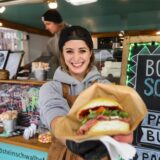 Eine Gastronomin zeigt einen Pastrami-Burger in die Kamera.