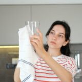 Eine Frau trocknet ein Glas mit einem Geschirrtuch ab.