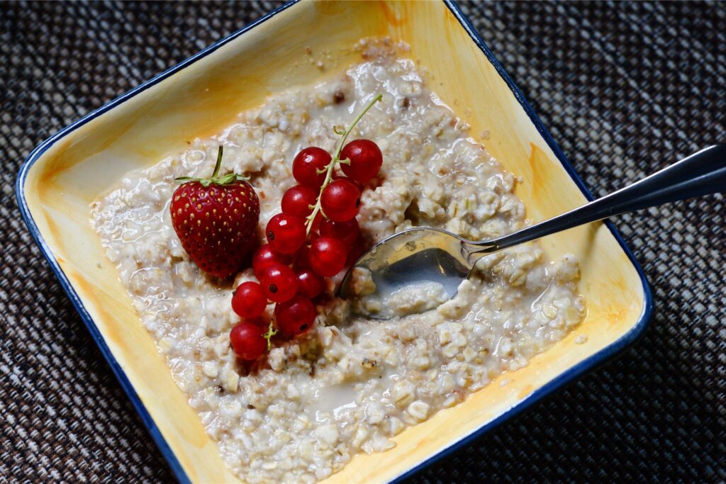 Eine Schale mit Porridge, die mit einer Erdbeere und Johannisbeeren garniert ist, steht auf einem Frühstückstisch. Eine Schale mit Porridge, die mit einer Erdbeere und Johannisbeeren garniert ist, steht auf einem Frühstückstisch.