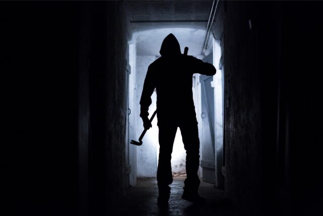 Die dunkle Silhouette einer Person mit Brechstange in der Hand steht in einem Gang.