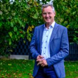 Axel Tschersich, SPD-Bürgermeisterkandidat aus Recklinghausen, steht mit blauem Sakko und Hemd in seinem Garten.