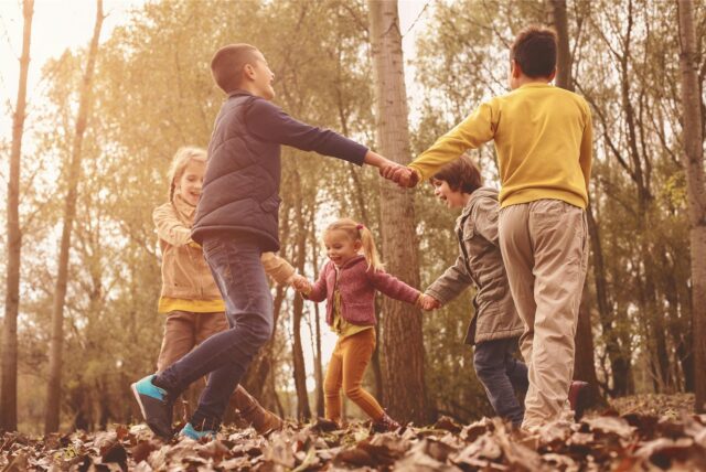 Fünf Kinder spielen an einem Herbsttag im Laub.