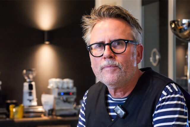 Thorsten Lohbeck sitzt in seiner Barista-Schule in der Lohnhalle der Zeche Ewald. Im Hintergrund sieht man die Scheiben der Lohnstelle, sowie eine Kaffeemühle und eine Kaffeemaschine.