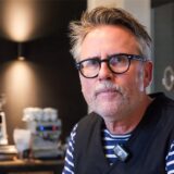 Thorsten Lohbeck sitzt in seiner Barista-Schule in der Lohnhalle der Zeche Ewald. Im Hintergrund sieht man die Scheiben der Lohnstelle, sowie eine Kaffeemühle und eine Kaffeemaschine.