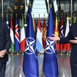 Mark Rutte steht links im Bild, rechts Jens Stoltenberg und spricht in ein Mikrofon. Zwischen ihnen stehen NATO-Flaggen.