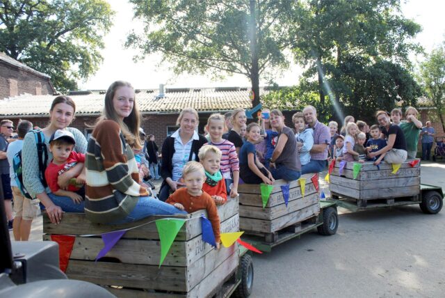Bild vom Erntedankfest 2023 im Spargeldorf: Eine Gruppe von Kindern und Erwachsenen sitzt auf drei Anhängern, und wartet darauf, dass der kleine Zug gleich durch die Apfelplantage auf dem Hof Schulte-Scherlebeck in der Hertener Ried fährt.