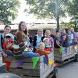 Bild vom Erntedankfest 2023 im Spargeldorf: Eine Gruppe von Kindern und Erwachsenen sitzt auf drei Anhängern, und wartet darauf, dass der kleine Zug gleich durch die Apfelplantage auf dem Hof Schulte-Scherlebeck in der Hertener Ried fährt.