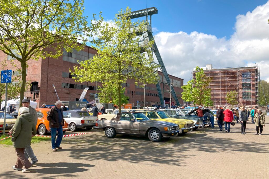 Auf dem Platz neben historischen Gebäuden der Zeche Ewald in Herten-Süd sind Oldtimer ausgestellt. Viele Männer und Frauen gehen an den parkenden Oldtimern vorbei. Auf dem Platz neben historischen Gebäuden der Zeche Ewald in Herten-Süd sind Oldtimer ausgestellt. Viele Männer und Frauen gehen an den parkenden Oldtimern vorbei.