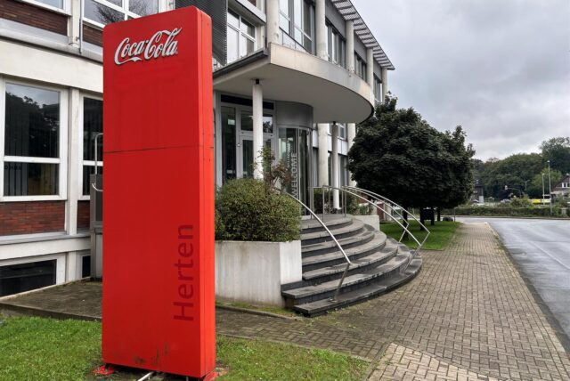 Der Eingangsbereich der Coca-Cola Zentrale in Herten an der Paschenbergstraße 30. Der Blick geht in Richtung Bahnlinie und Innenstadt. Auf der großen roten Bande steht Coca Cola Herten.