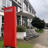 Der Eingangsbereich der Coca-Cola Zentrale in Herten an der Paschenbergstraße 30. Der Blick geht in Richtung Bahnlinie und Innenstadt. Auf der großen roten Bande steht Coca Cola Herten.