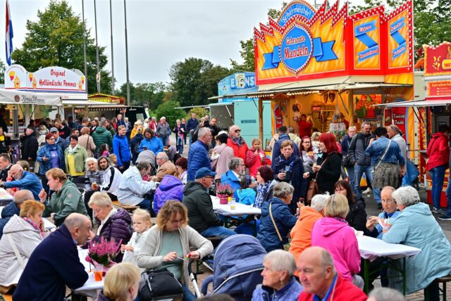 Besucher sitzen beim Seefeest in Marl an Tischen, die zwischen Imbissbuden aufgebaut sind.