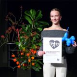 Wioletta Litvinov steht mit einer Urkunde und einem blauen Luftballon in den Händen auf der Bühne der Stadthalle Datteln.