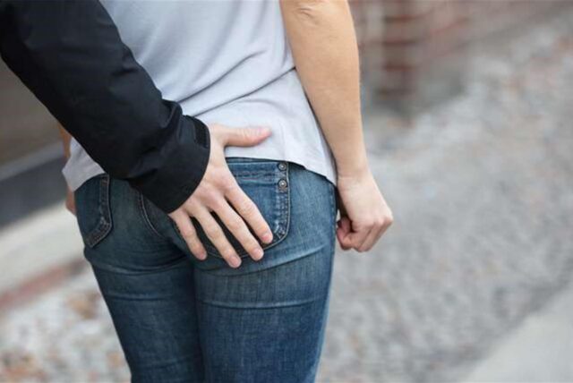 Eine Hand greift einer jungen Frau von hinten an de Po.