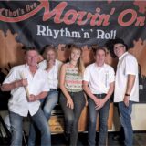 Die Band Movin’On steht und sitzt vor einem Banner mit der Aufschrift „Movin’On – Rhythm’n’Roll“.