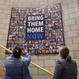 Zwei Frauen stehen vor einem Plakat mit der Aufschrift „Bring them home now“, eine fotografiert es mit ihrem Handy.