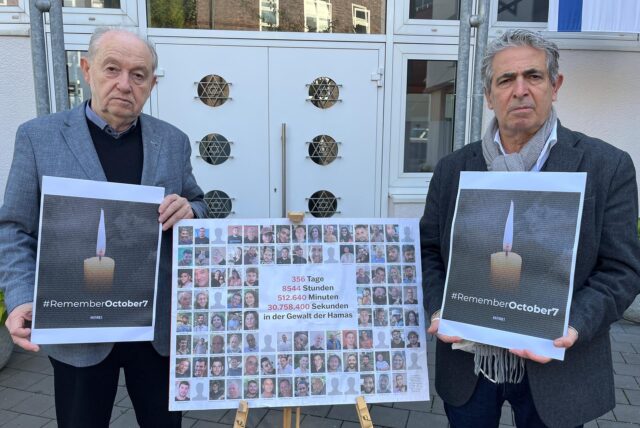 Dr. Mark Gutkin (links), Vorsitzender der Jüdischen Gemeinde Recklinghausen, und Vorbeter Isaac Tourgman stehen vor der Synagoge. Zwischen ihnen steht eine Staffelei mit einer Collage der beim Überfall der Hamas auf Israel entführten Personen. In den Händen halten die beiden Männer Bilder einer Kerze, darunter steht #RememberOctober7.