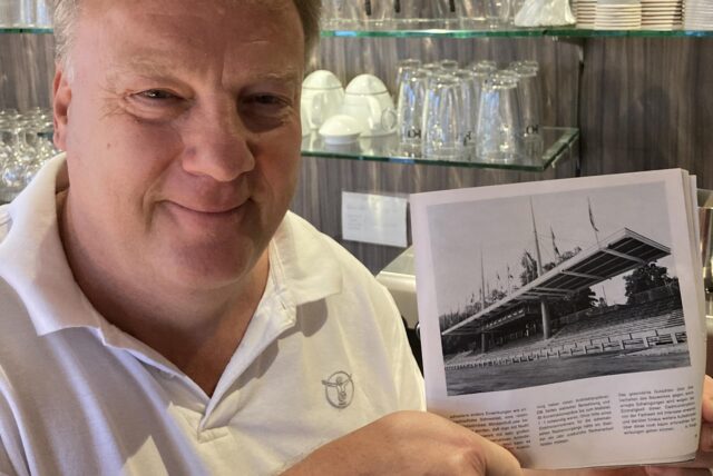 Café-Inhaber Peter Tudyka zeigt die Festschrift zum 50-jährigen Bestehen des TSV Marl-Hüls, in der eine alte Aufnahme der Tribüne im Jahnstadion zu sehen ist.
