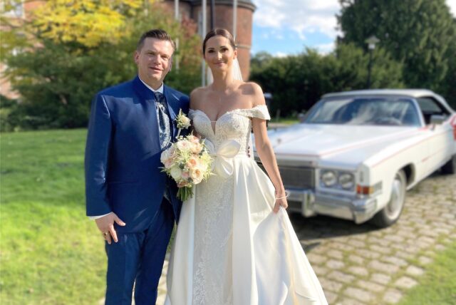 Dr. Michael und Isabell Schymura stehen nach ihrer kirchlichen Trauung in der Hertener Schlosskapelle vor einem Oldtimer.
