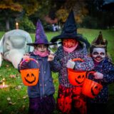 Gruselig verkleidete Kinder stehen an Halloween auf einer Wiese vor einem großen Tier-Skelett.