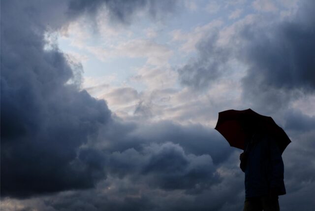 Ein Mann geht mit einem Regenschirm vor aufziehenden dunklen Wolken spazieren.