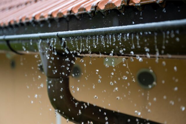 Regen tropft von einer Dachrinne.