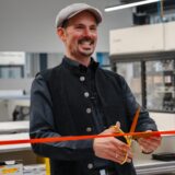 Jörg Baumeister durchtrennt mit einer goldenen Schere ein rotes Band.