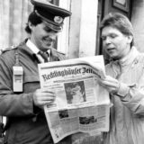 Zwei Männer, einer davon in Polizeiuniform, lesen die Recklinghäuser Zeitung. Es handelt sich um eine Schwarz-Weiß-Aufnahme.