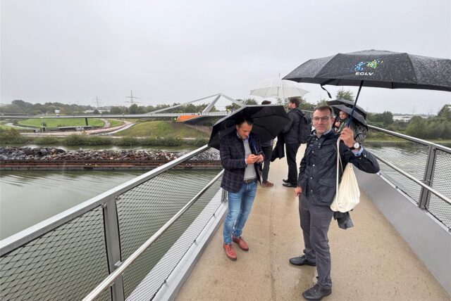 Architekt Falko Schmitt (r.) und Kollegen schauen sich „ihr“ Bauwerk Sprung über die Emscher kurz nach der Freigabe unterm Regenschirm an.