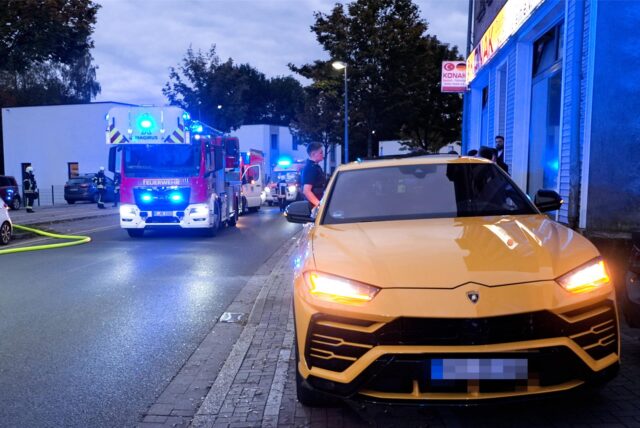 Ein gelber Sportwagen steht auf einem Geh- und Radweg, dahinter Feuerwehrleute im Brandeinsatz in Herten.