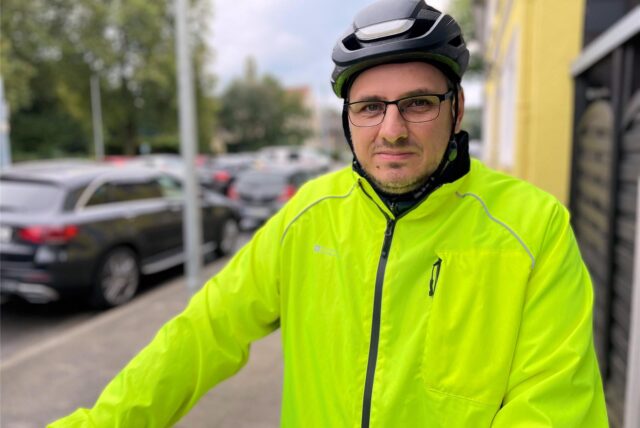 Patrick Berner steht mit Fahrradhelm und grüner Jacke auf dem Bürgersteig.