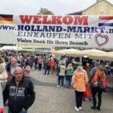 Hollandmarkt auf dem Tigg, über den Ständen hängt ein Banner: „Welkom Holland-Markt Einkaufen mit Herz. Vielen Dank für Ihren Besuch“