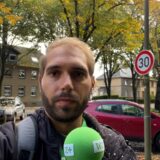Reporter Daniel Brill steht mit einem Mikrofon in der Hand an der Waltroper Riphausstraße. Im Hintergrund parkt ein Auto neben einem Mast, an dem ein Tempo-30-Schild hängt.