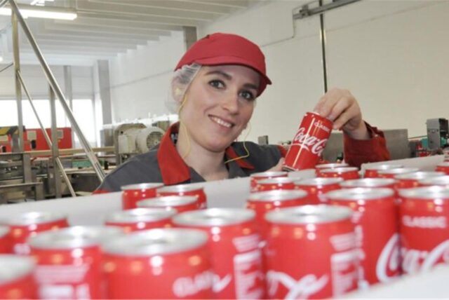 Frau hält in eine Produktionshalle eine Coca-Cola-Dose in der Hand