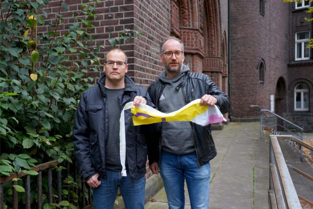 Tobias Ahlendorf vom Kirchenvorstand der Heilig-Kreuz-Gemeinde (links) und Studierendenpfarrer Dr. Simon Schwamborn (KHG) fanden von der Regenbogenfahne an der Heilig-Kreuz-Kirche nur noch einen Fetzen Stoff.