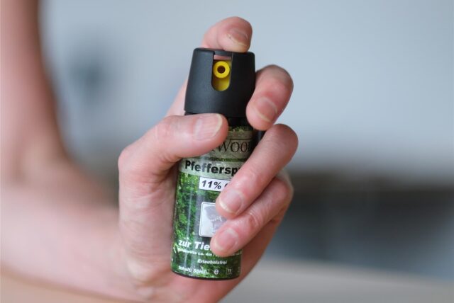 Eine Person hält eine Pfefferspraysprühdose in die Kamera.