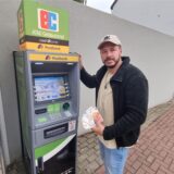 Ein Mann steht an einem Geldautomaten und hält Geldscheine in der Hand.