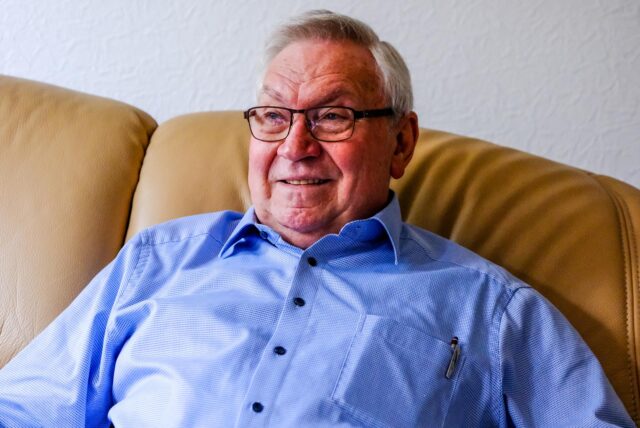 Ein Porträt von Heinz Budde, der auf einem braunen Sofa sitzt.