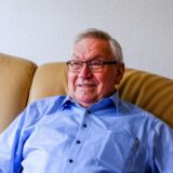 Ein Porträt von Heinz Budde, der auf einem braunen Sofa sitzt.