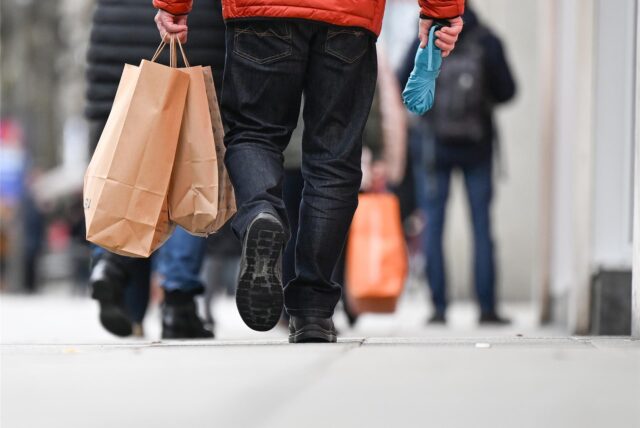 Ein Mann geht am verkaufsoffenen Sonntag mit Einkaufstüten durch eine Einkaufsstraße.