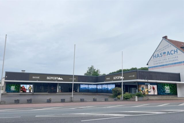 Ehemalige McTrek-Filiale in Datteln mit neuen Schildern mit der Aufschrift „Outdoor Sports Outlet“, an den Fenstern sind große Fotos angebracht und eine Berglandschaft, auf der verschiedene Sportarten dargestellt sind.